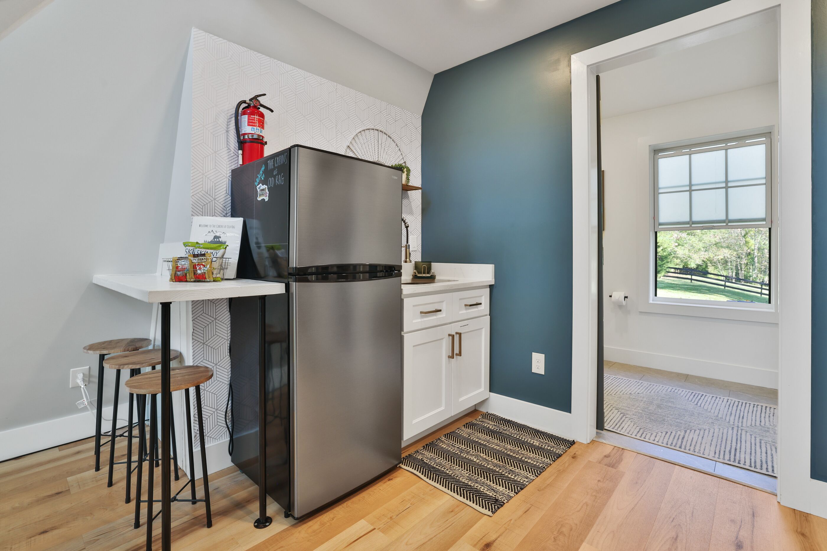A modern kitchen with a stainless steel refrigerator, white cabinetry, and a small bar area with stools.