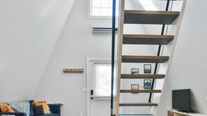 Un espacio tipo loft con suelo de madera, un sofá azul, una escalera y un televisor.