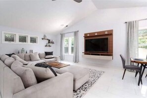 Relax in this stylish living room with a large sofa, flat-screen TV, and dining area.