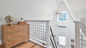 Une chambre de style loft moderne, avec une commode en bois, un ventilateur, une fenêtre à motifs géométriques et un luminaire au plafond original.