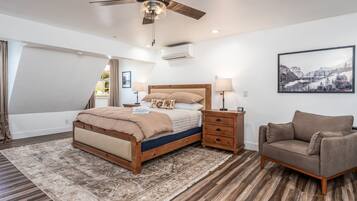 A bedroom with a bed, bedside tables, a chair, a ceiling fan, and a large window.