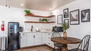 Una cocina moderna con armarios blancos, un refrigerador de acero inoxidable, una mesa de comedor de madera con sillas y cuadros en la pared.