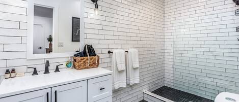 Une salle de bain moderne avec des carreaux de métro blancs, un lavabo blanc avec des robinets noirs, des toilettes blanches et un petit espace douche.