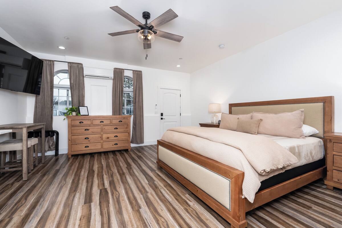 Un dormitorio con cama, cómoda de madera, escritorio y ventilador de techo.