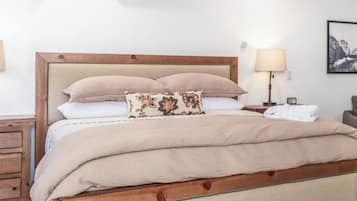 Una cama bien hecha con estructura de madera y ropa de cama color crema, una mesita de noche con una lámpara y un aire acondicionado instalado en la pared.