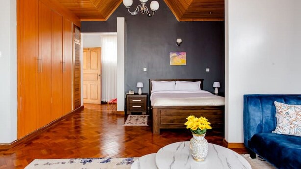 Een kamer met een houten plafond, een bed met wit beddengoed, een blauwe bank en een marmeren tafel met een bloevas.
