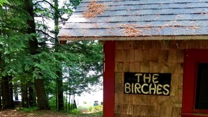 Una pequeña cabaña de madera con un cartel que dice "THE BIRCHES" en el costado.