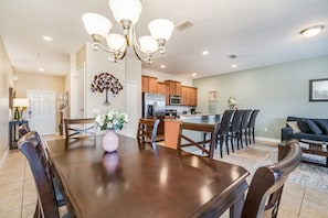 A spacious dining area with a large wooden table and chairs, a chandelier, and a kitchen in the background. - Lovely Town Home with Splash Pool-8944CPR (Kissimmee)
