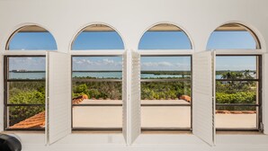 A room with three arched windows overlooking a beach and water.