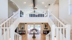 A spacious interior with a central open-plan area, a staircase with white railings, and a ceiling fan.