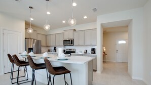 A modern kitchen with white cabinetry, stainless steel appliances, and a central island with bar stools. - Beautiful Town Home with Splash Pool-8916SA (Kissimmee)