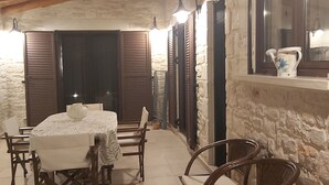 Un coin repas chaleureux avec une table ronde et des chaises, des murs en pierre, des poutres en bois et une fenêtre agrémentée d’un objet décoratif.