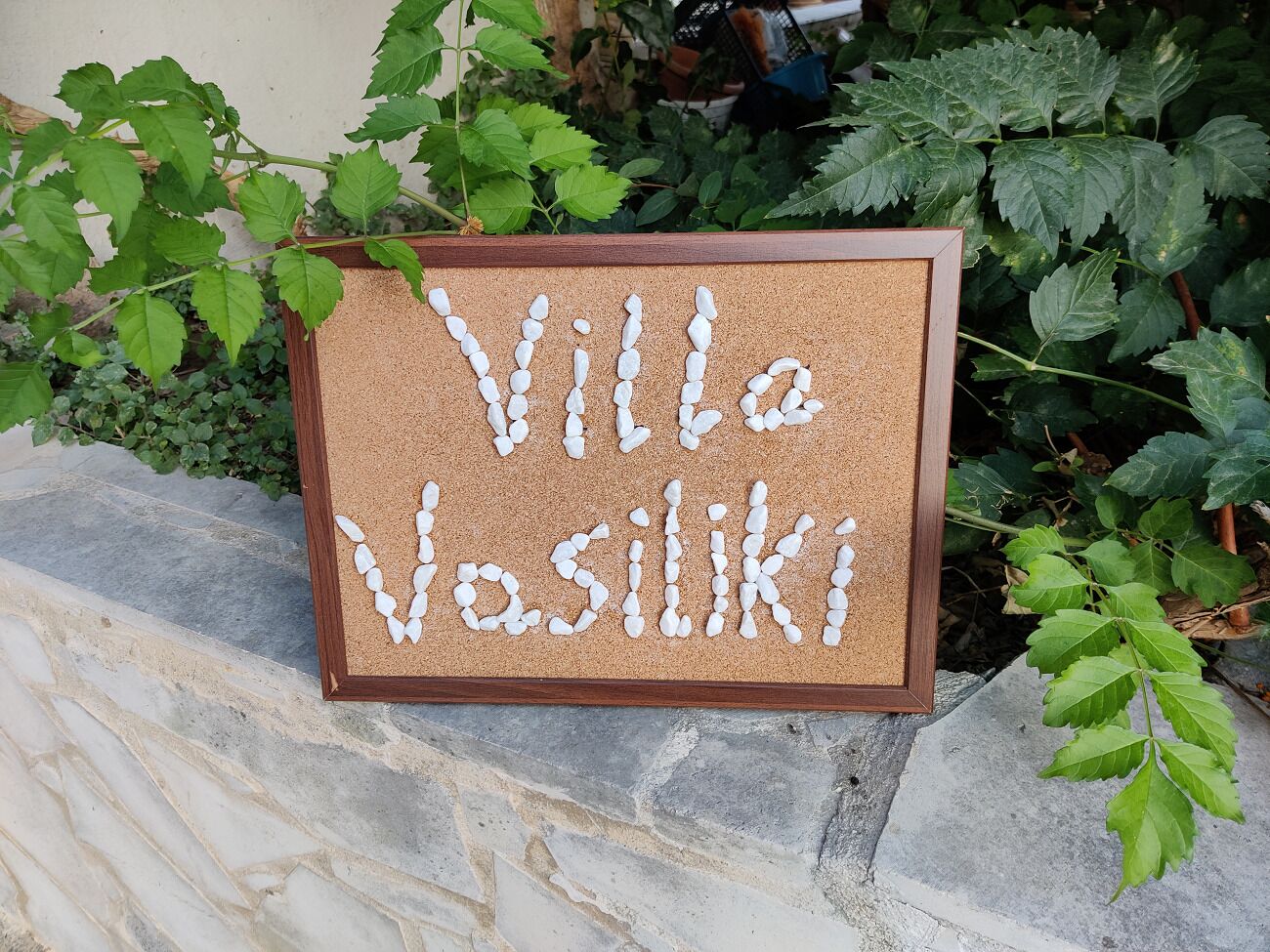 Een prikbord met de naam 'Villa Vasilikos' geschreven met witte kiezelstenen.