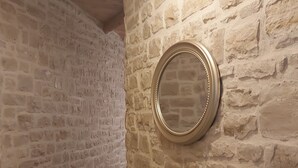 Un couloir aux murs de pierre et orné d’un miroir rond sur l’un des murs.