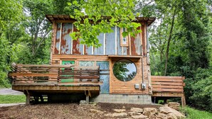 Une cabane rustique dotée d’une terrasse en bois et d’une fenêtre circulaire.