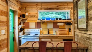 Une cuisine rustique avec des murs en bois, une porte verte, une grande fenêtre et un coin repas équipé de deux tabourets.