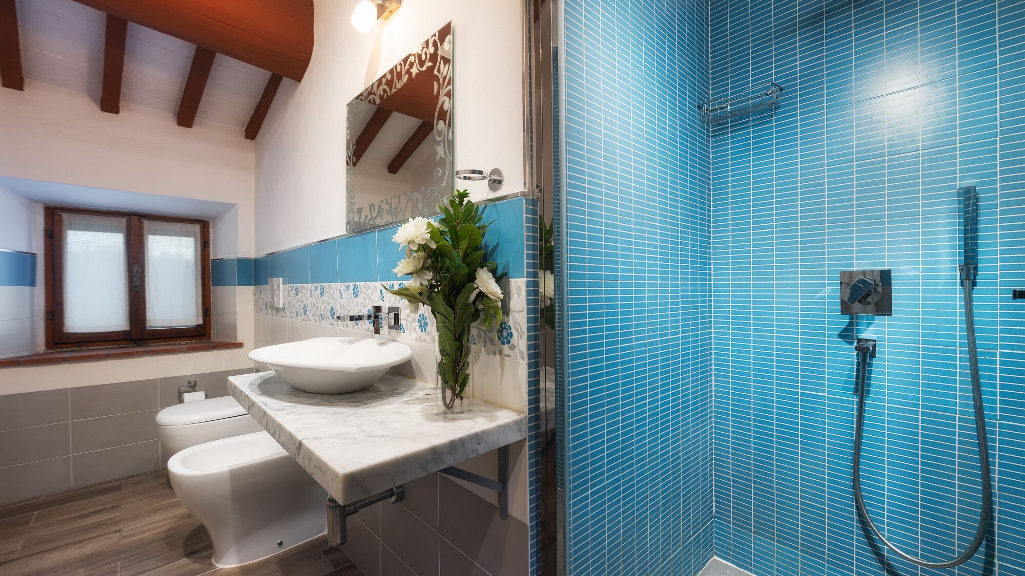 A bathroom with a white sink, a toilet, and a shower with blue tiles.
