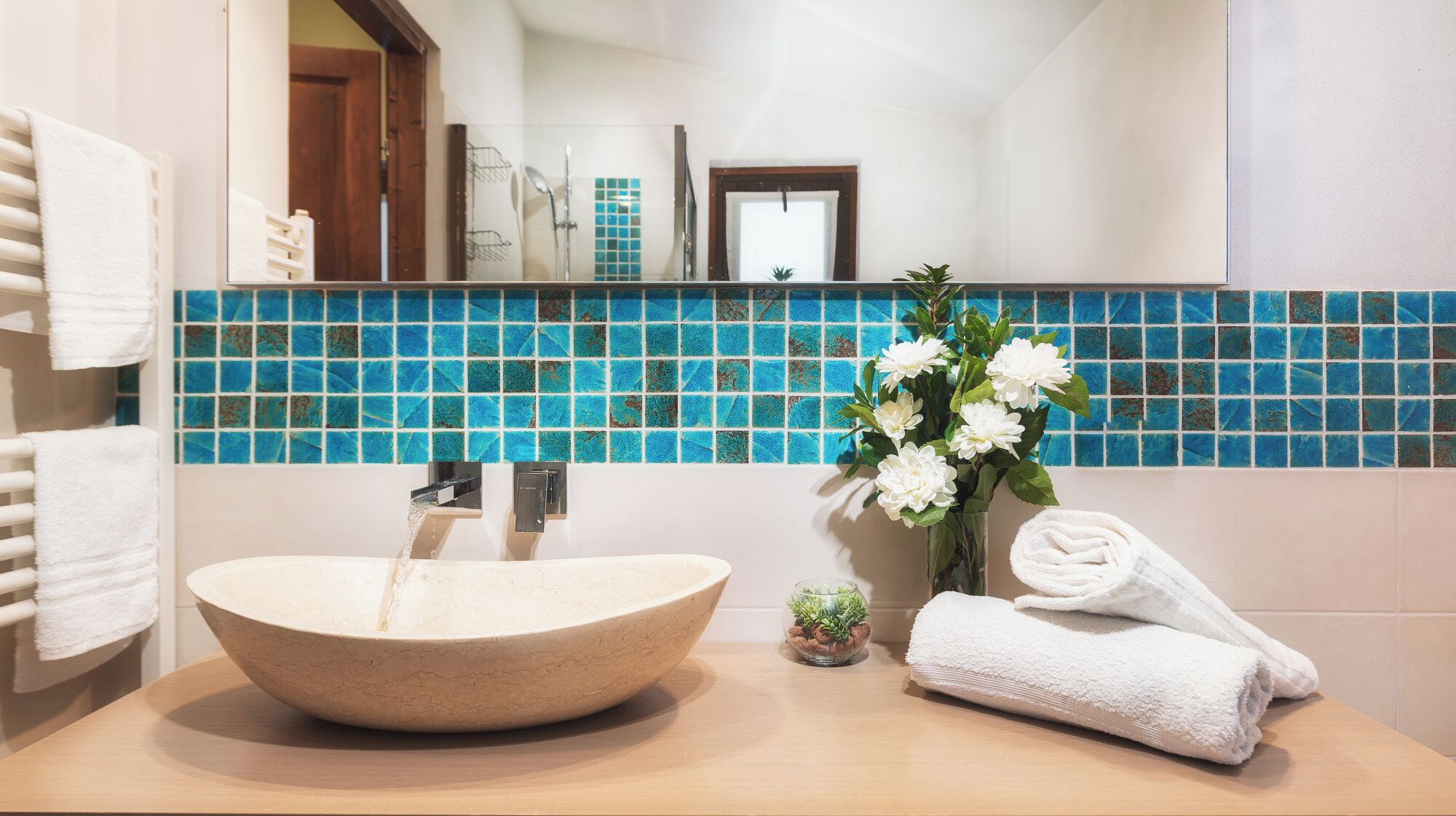 Une salle de bain avec un grand lavabo en forme de coupe, un miroir, un pare-chocs bleu en carreaux, une petite plante en pot et une serviette enroulée posée sur le comptoir.