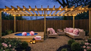 Ein Garten mit einer Holz-Pergola, einem Whirlpool, zwei Korbsesseln und einem Tisch mit Kissen.