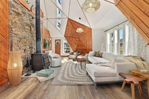 Ett mysigt vardagsrum med en vägg av sten, en öppen spis, en vit soffa och en hängande lampa.