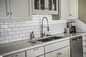 Una cocina con armarios blancos, un lavamanos de acero inoxidable y una cafetera.