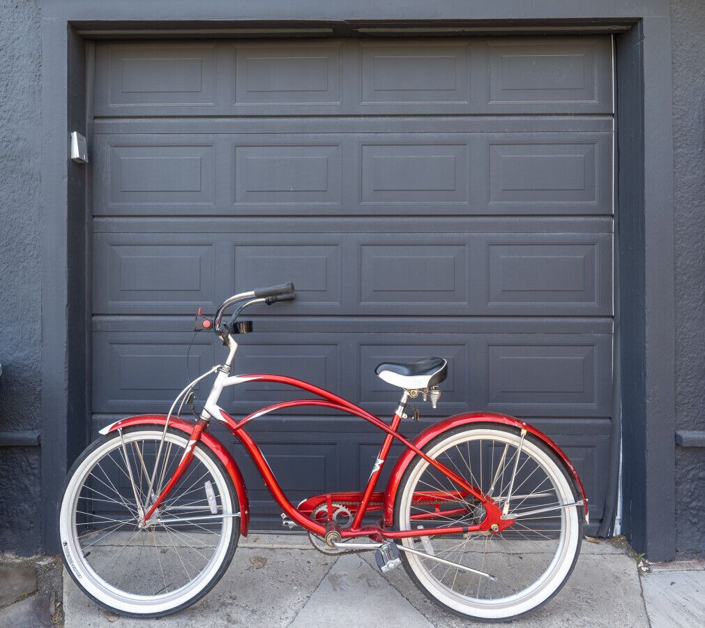 Una bicicleta roja estacionada frente a una puerta de garaje gris oscuro.