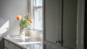 Ett badrum med ett vitt handfat, en vas med blommor och ett fönster.