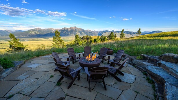 A stone patio with a fire pit and Adirondack chairs overlooking a mountainous landscape. - Experience Luxury in Nature: Private Lodge & Guest Home in Paradise Valley (Emigrant)