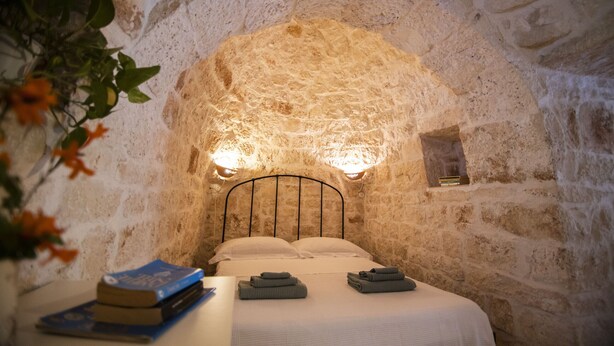 Un dormitorio con paredes de piedra, una cama, almohadas y toallas dobladas.