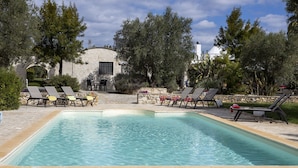 Una piscina rectangular con sillones de descanso y un muro de piedra.