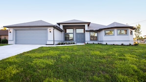 A modern two-story house with a garage, a front porch, and a well-maintained lawn. - Gulf Access Getaway: Sleeps 10, Private Pool & Boat Rental Option. (Cape Coral)
