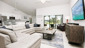 A modern living room with a sectional sofa, a coffee table, and a TV mounted on the wall. - Gulf Access Getaway: Sleeps 10, Private Pool & Boat Rental Option. (Cape Coral)