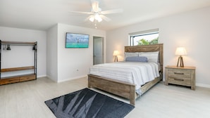 A bedroom with a bed, bedside tables, a ceiling fan, a TV, and a window with a view. - Gulf Access Getaway: Sleeps 10, Private Pool & Boat Rental Option. (Cape Coral)