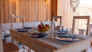 Una mesa de madera para cuatro personas, con platos, vasos y un cuenco de fruta.