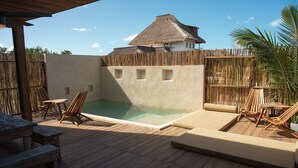 Una terraza de madera con piscina, sillas de descanso y un edificio con techo de paja.