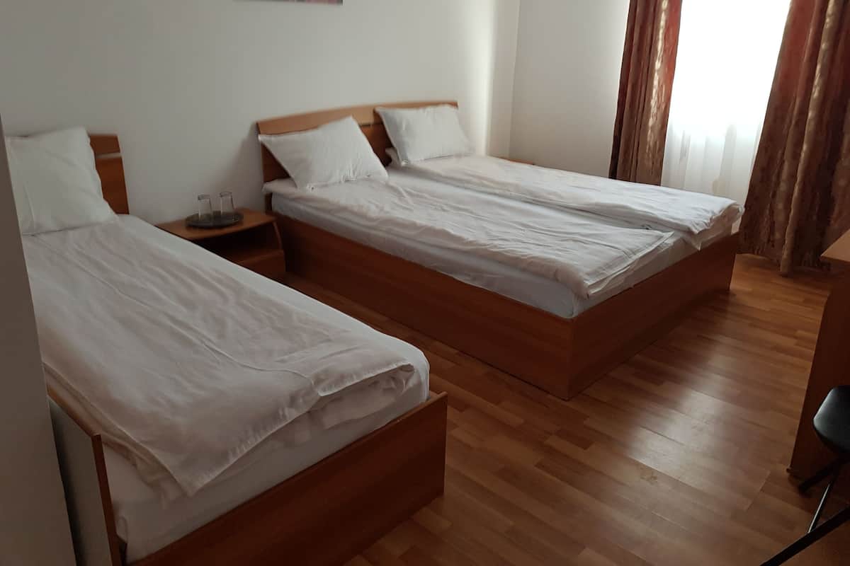 A hotel room with two single beds, wooden headboards, white bedding, a nightstand with a glass, and a painting on the wall.