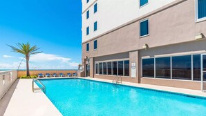 A swimming pool with lounge chairs and a palm tree, adjacent to a building with large windows. - EAST CORNER CONDO DIRECT GULF VIEW/2 BEDROOM & 2 BATH/CLOSE 2 PIER (Gulf Shores)