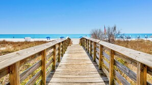 A wooden boardwalk leading to a beach with umbrellas and a flag. - EAST CORNER CONDO DIRECT GULF VIEW/2 BEDROOM & 2 BATH/CLOSE 2 PIER (Gulf Shores)