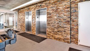 An elevator area with a brick wall, two elevators, and a car entrance. - EAST CORNER CONDO DIRECT GULF VIEW/2 BEDROOM & 2 BATH/CLOSE 2 PIER (Gulf Shores)
