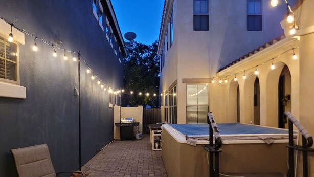 A patio area with a barbecue grill, a small table with a patterned tablecloth, and string lights.
