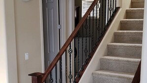 A staircase with a wooden handrail and black balusters, leading to a landing with a door and a light fixture.