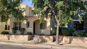 A two-story house with a beige facade, a red-tiled roof, and a front entrance with steps.