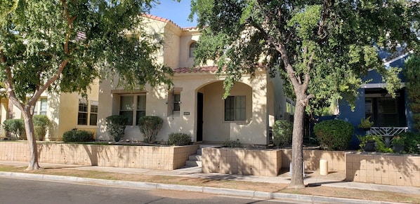 Una casa de dos pisos con fachada color beige, techo de tejas rojas y entrada principal con escalones.