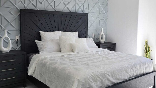 Ein modernes Schlafzimmer mit einem dunklen Holzbett, weißer Bettwäsche und einer Wand mit geometrischem Muster.