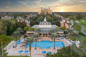 A resort with a large pool, palm trees, and a view of a distant building at sunset.