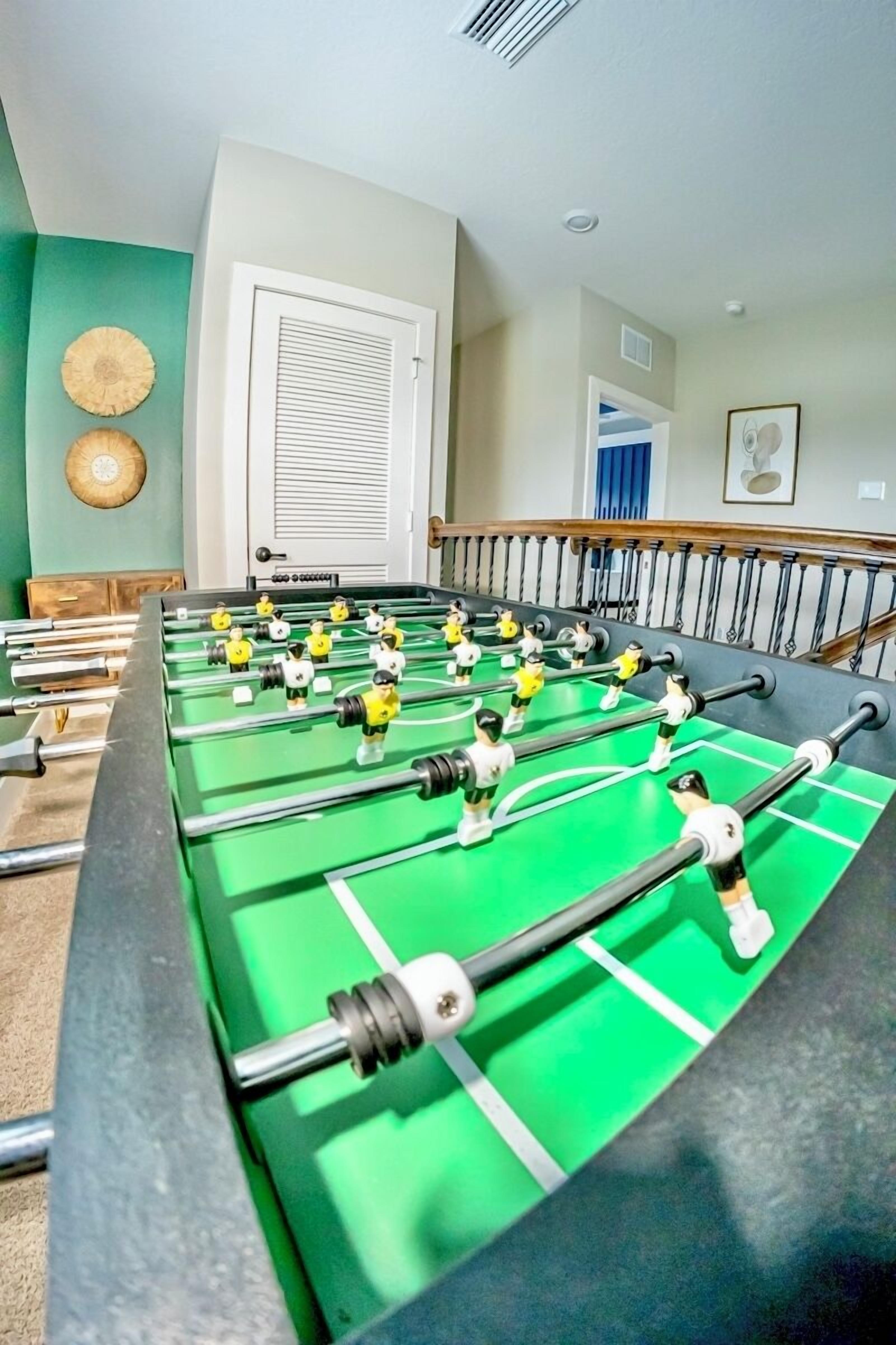 A foosball table in a room with a door, a wall clock, and a framed picture.