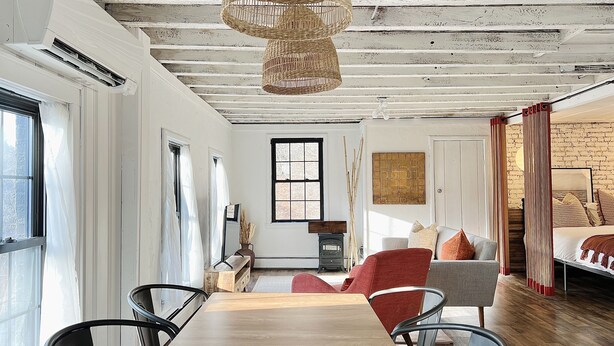 A modern living room with a wooden dining table, red and grey chairs, a wicker chandelier, and a brick wall. - Bohemian style open LOFT (Kingston)