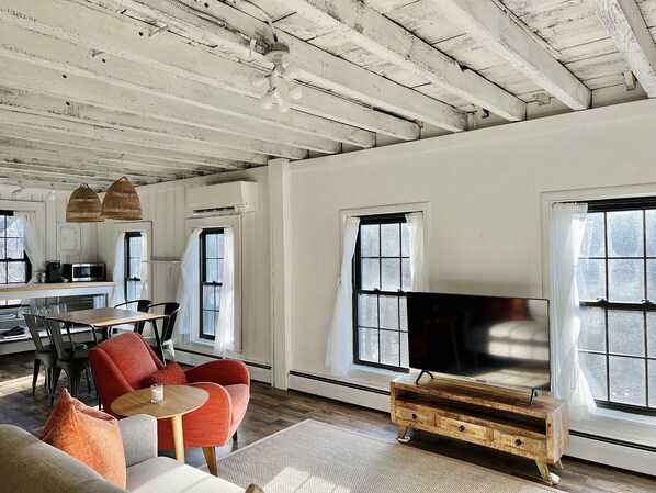 A spacious living room with a large TV, wooden furniture, and a kitchen area with a microwave. - Bohemian style open LOFT (Kingston)