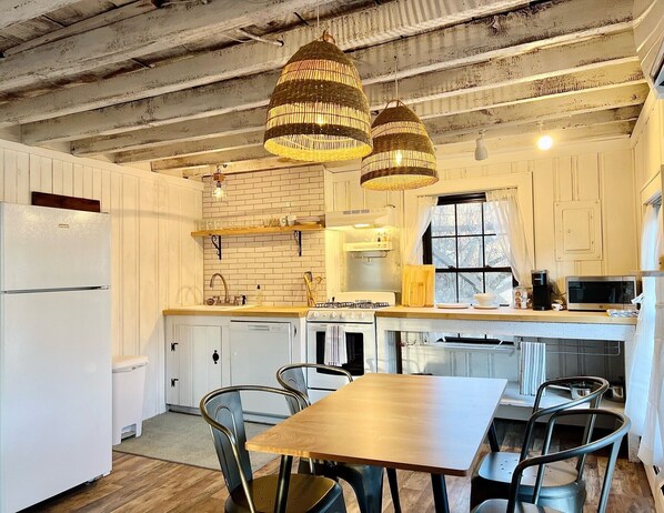 A kitchen with white cabinets, a wooden table, and hanging wicker chandeliers. - Bohemian style open LOFT (Kingston)