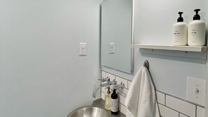 A bathroom with a stainless steel sink, a mirror, a towel hanging on the wall, and two bottles of lotion on a shelf. - Bohemian style open LOFT (Kingston)